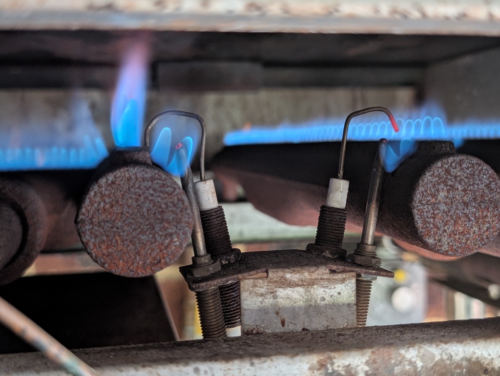 Atmospheric burner assembly showing standing pilot flame impingement, glowing thermocouple hot junction, and flame sensing probe